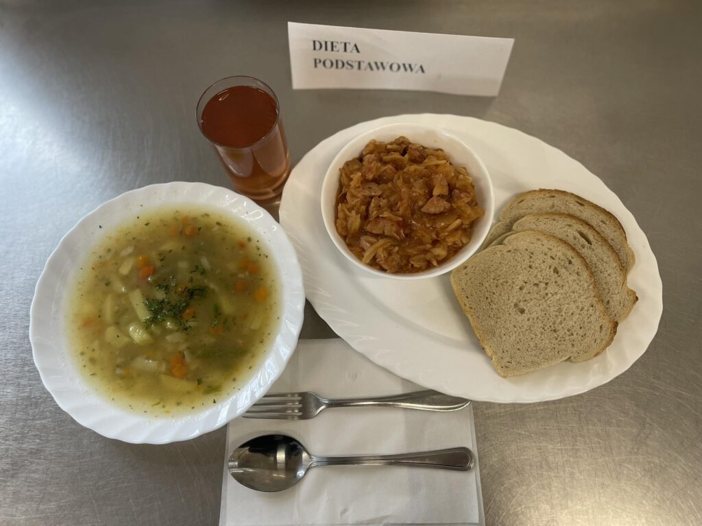 zdjęcie obiadu złożonego z: zupy jarzynowej, bigosu, chleba oraz kompotu.