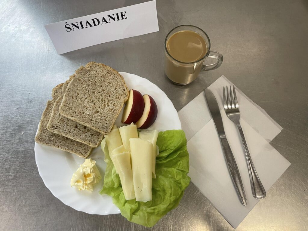 zdjęcie śniadania złożonego z: sera twardego, chleba razowego, margaryny oraz kawy z mlekiem.