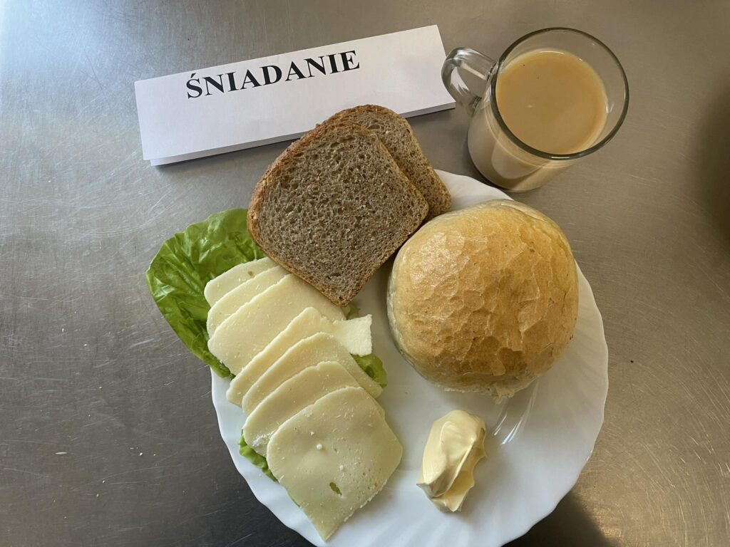 zdjęcie śniadania złożonego z: sera twardego, bułki, margaryny, chleba oraz kawy z mlekiem.