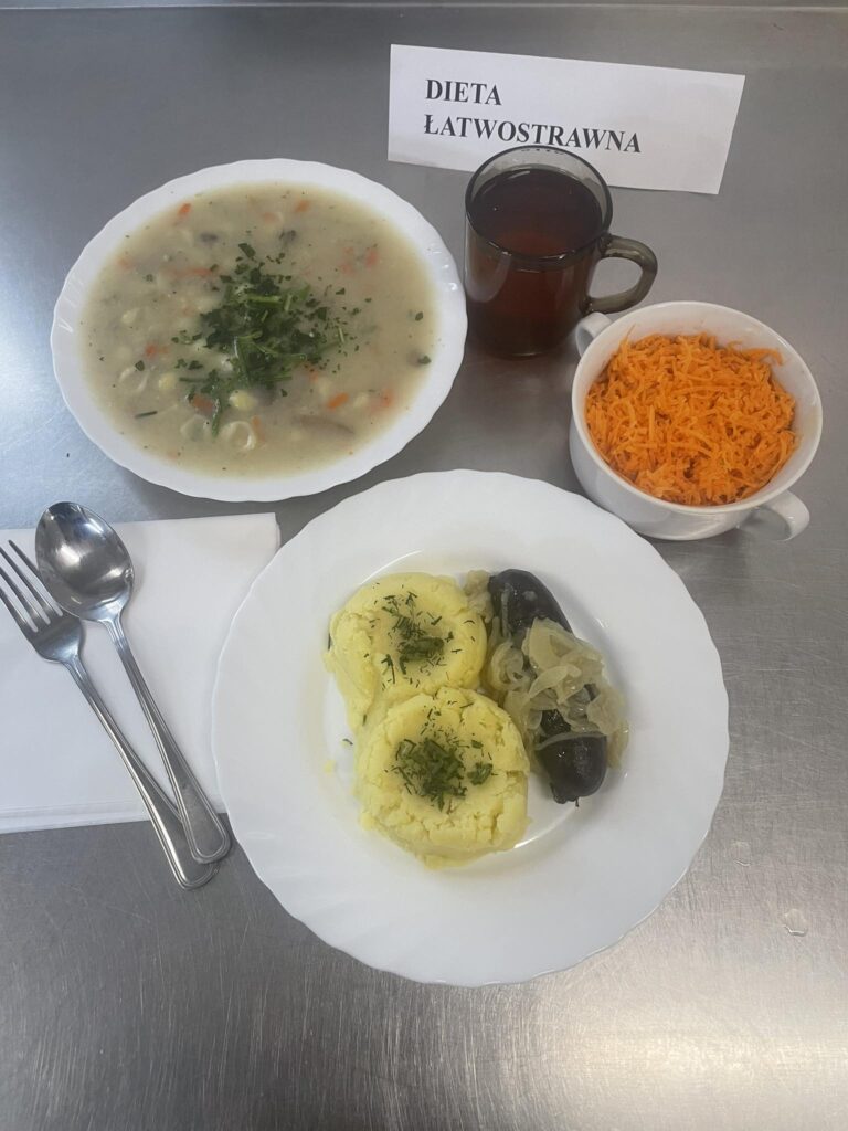zdjęcie obiadu złożonego z; zupy pieczarkowej z makaronu, kiszki gryczanej, ziemniaków, surówki z marchwi kiszonej oraz kompotu.