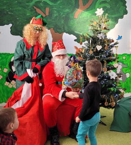 zdjęcie przedstawia elfa z św. Mikołajem ora z małym chłopczykiem odbierającym swój prezent.