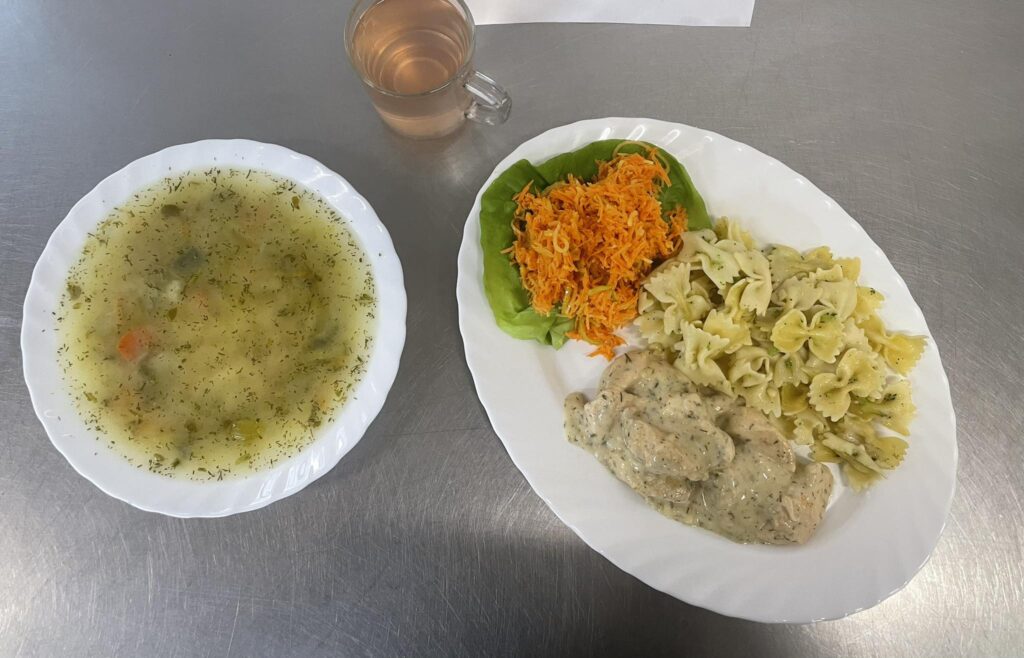 zdjęcie obiadu złożonego z; zupy ogórkowej z ryżem, makaronem penee z kurczakiem w sosie serowym, surówki z marchwi i pory oraz kompotu.