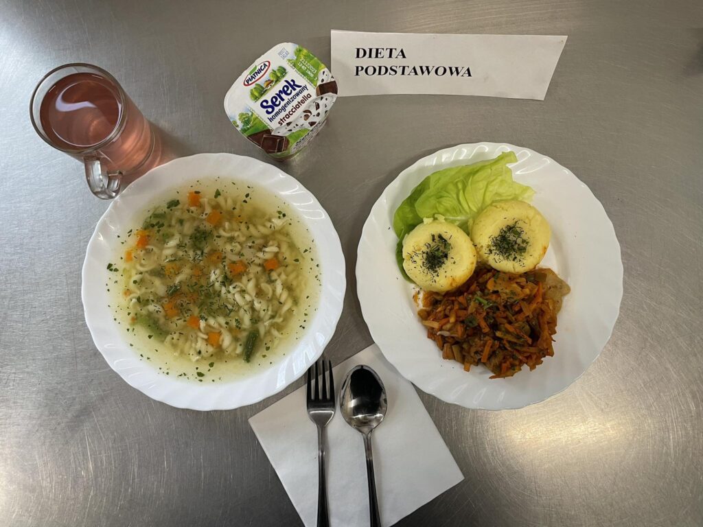 zdjęcie obiadu złożonego z: zupy makaronowej, ryby pieczonej z warzywami, ziemniaków oraz kompotu.na zdjęciu również podwieczorek czyli serek homogenizowany.