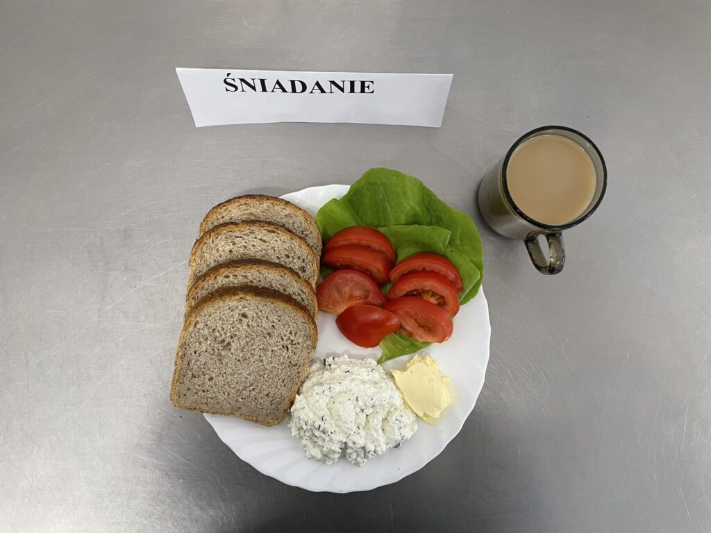 zdjęcie śniadania złożonego z: twarogu z koperkiem, chleba, pomidora, margaryny oraz kawy zbożowej.