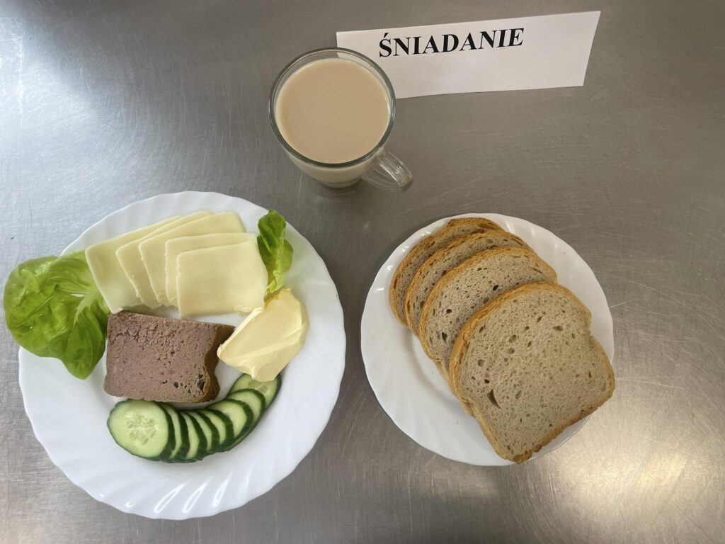 zdjęcie śniadania złożonego z: pasztetu pieczonego, ogórka, sera żółtego, chleba, margaryny oraz kawy zbożowej.