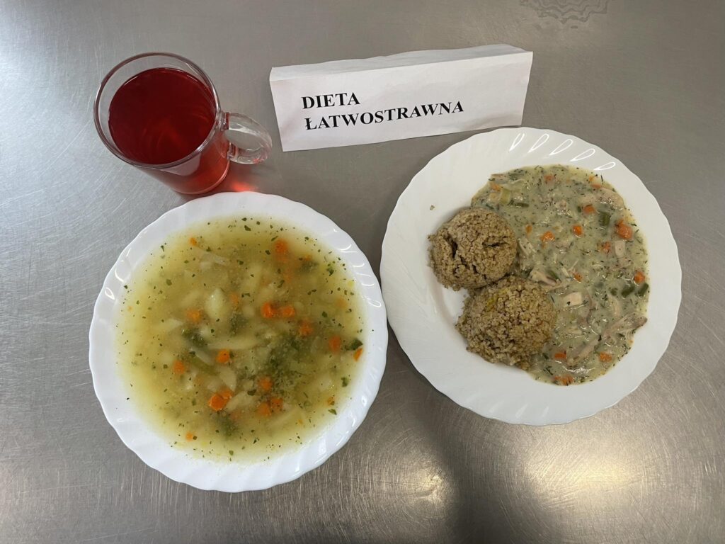 zdjęcie obiadu złożonego z: zupy jarzynowej, potrawki wieprzowej, chleba oraz kompotu.