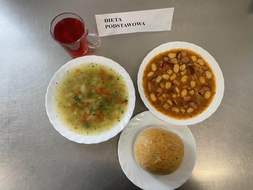 zdjęcie obiadu złożonego z: zupy jarzynowej, fasolki po bretońsku, chleba oraz kompotu.