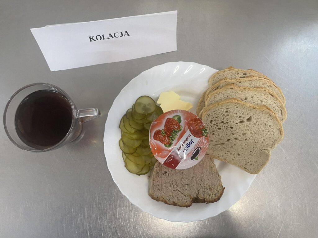 zdjęcie kolacji złożonej z: pasztetu pieczonego, ogórka kiszonego, chleba, margaryny oraz herbaty.