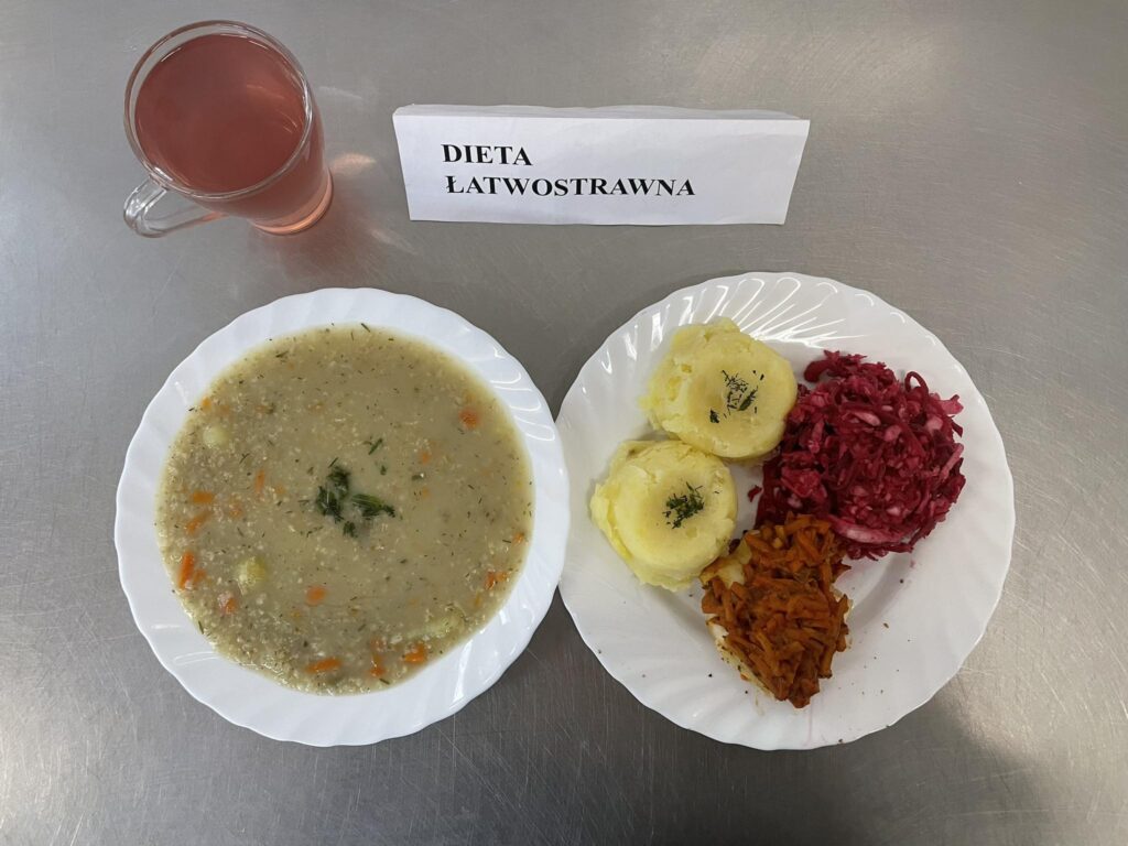 zdjęcie obiadu złożonego z: zupy krupnik, ryby pieczonej z warzywami, ziemniaków, surówki z kapusty i buraka oraz kompotu.