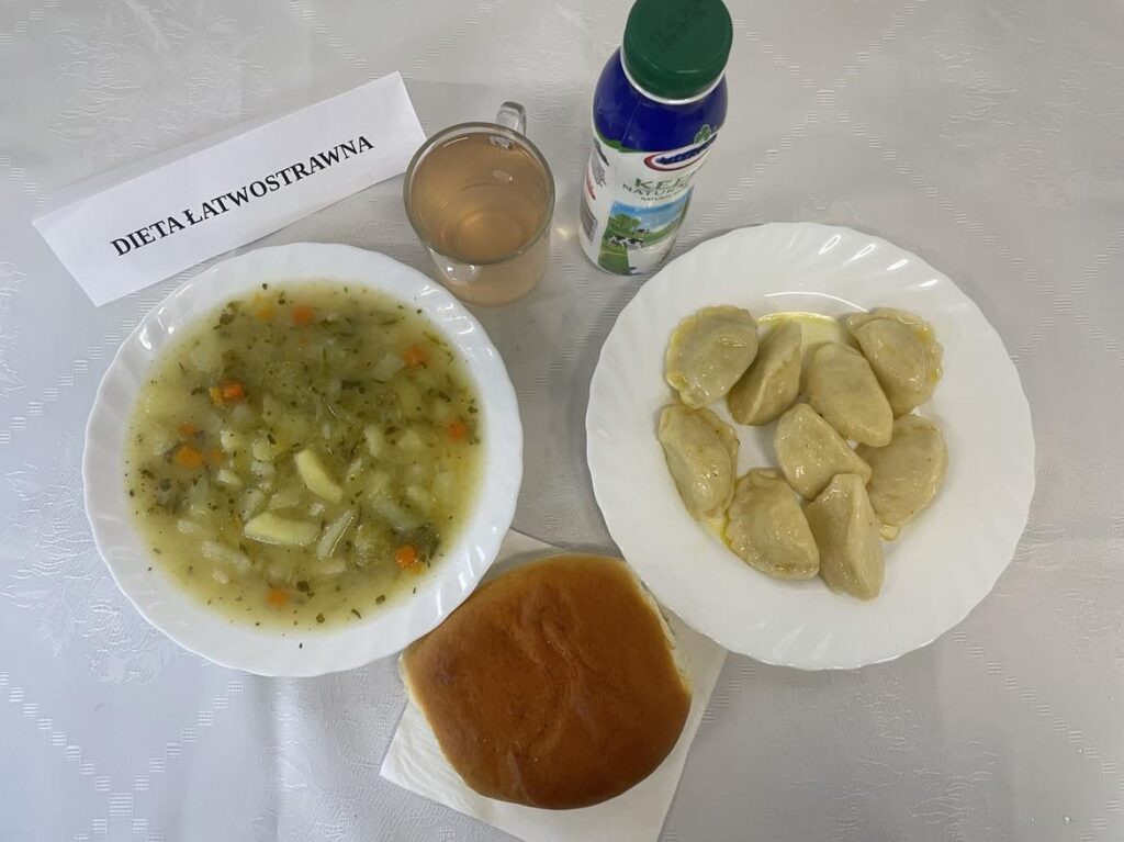 Zdjęcie obiadu złożonego z: zupy kalafiorowej z makaronem, pierogów, kefiru, kompotu oraz drożdżówki na podwieczorek.
