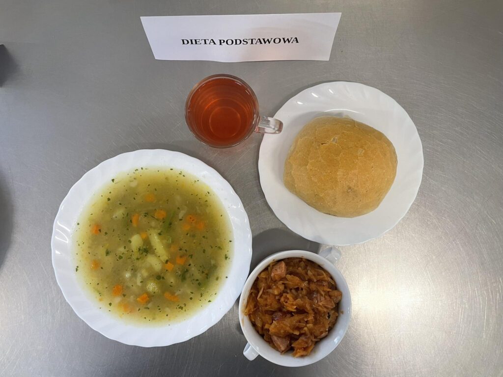 Zdjęcie obiadu złożonego z: zupy jarzynowej, bigosu, bułki oraz kompotu.