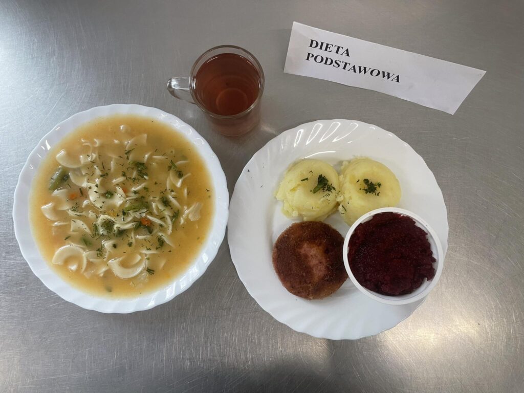 zdjęcie z obiadem złożonym z: zupy ogonowej z makaronem, mortadeli panierowanej, ziemniaków, ćwikły oraz kompotu.