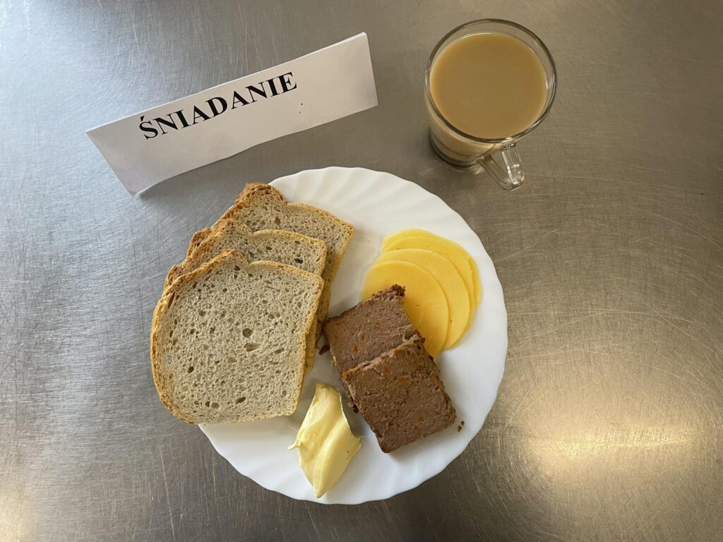 Śniadanie złożone z:pasztetu pieczonego, sera twardego, chleba, margaryny oraz kawy z mlekiem.