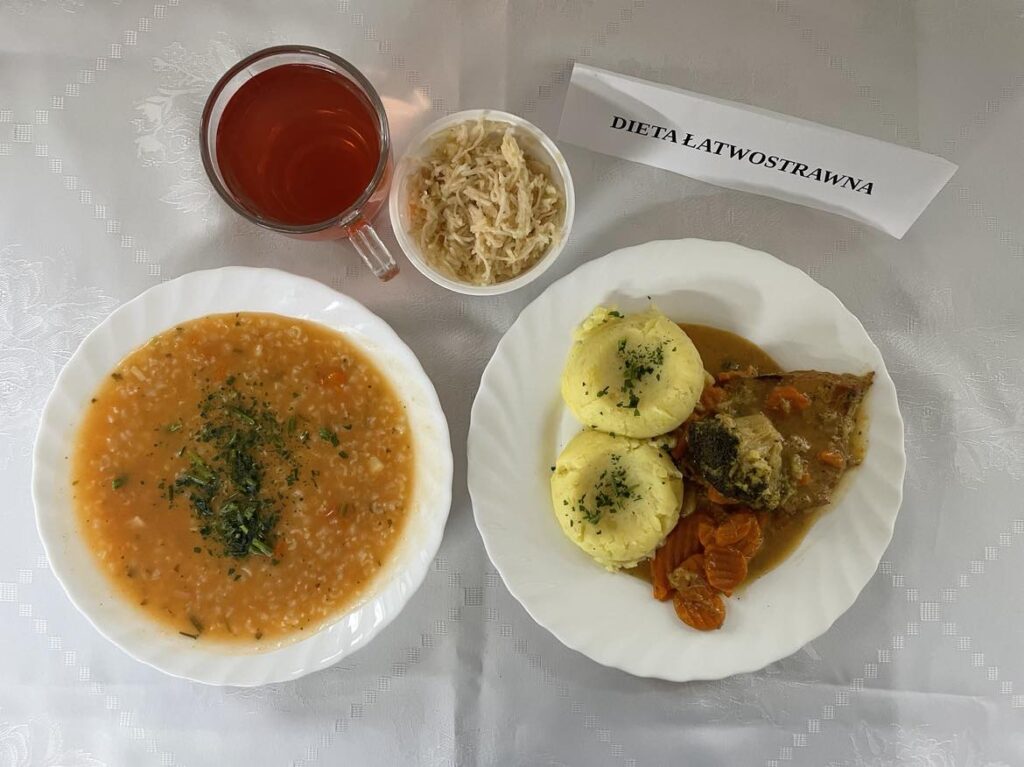 zdjęcie obiadu złożonego z: zupy pomidorowej z ryżem, schabem duszonym w warzywach, ziemniakami puree, surówki z selera i jabłka oraz kompotu z jabłek.