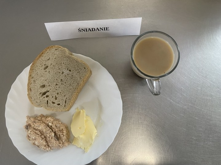 Śniadanie złożone z: chleba mazowieckiego, margaryny śniadaniowej, pasty z makrelą i twarożkiem oraz kawą zbożowa z mlekiem.