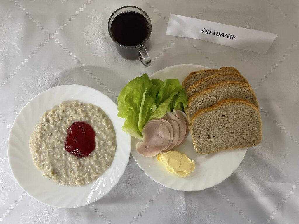 Zdjęcie śniadania złożonego z: owsianki z dżemem, chleba mazowieckiego, szynki kanapkowej, margaryny śniadaniowej, papryki czerwonej oraz herbaty.