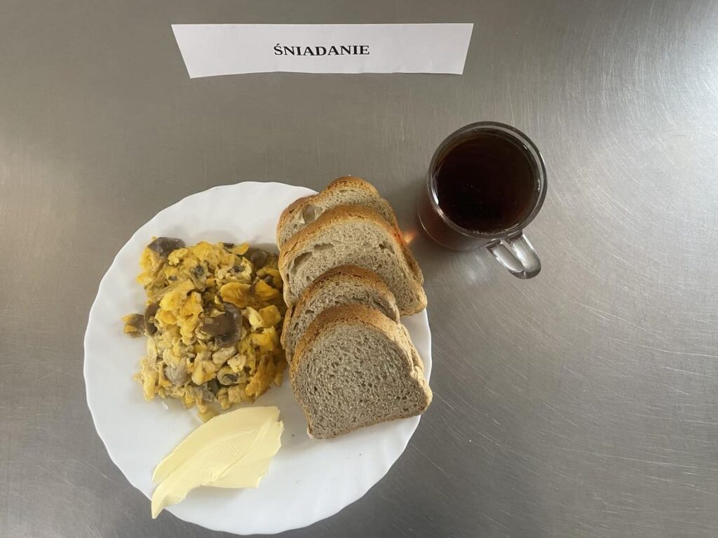 Śniadanie złożone z: chleba mazowieckiego oraz razowego, margaryny, jajecznicy z pieczarkami oraz herbaty czarnej.