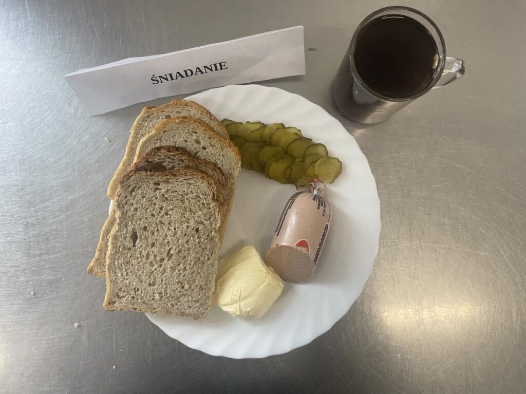 Śniadanie złożone z: chleba mazowieckiego oraz razowego, margaryny, pasztetu, ogórka oraz herbaty.
