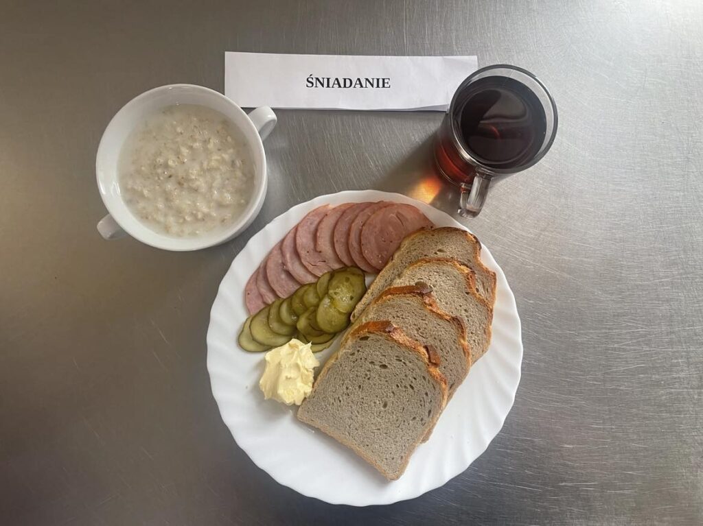 Śniadanie złożone z: chleba pszennego, margaryny, ogórka konserwowego, kiełbasy krakowskiej oraz herbaty.