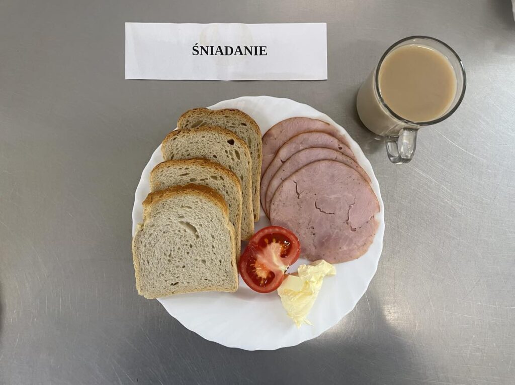 Śniadanie złożone z :chleba pszennego, margaryna śniadaniowa, szynki kanapkowej, pomidora oraz kawy zbożowej.