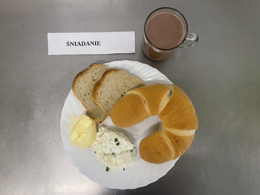Śniadanie złożone z: chleba pszennego, margaryny śniadaniowej, twarożku ze szczypiorkiem, klasyczne kakao, bułki i rogale maślane.