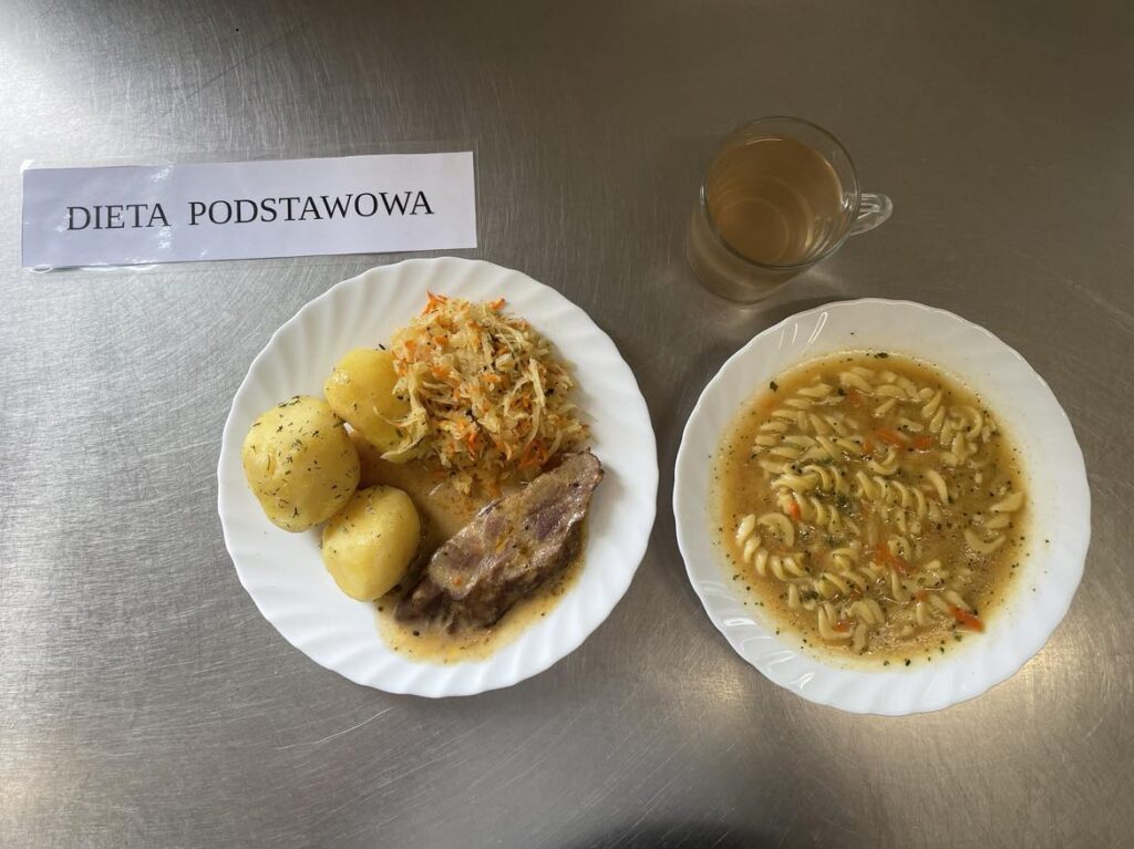 Obiad złożony z: zupy szpinakowej z ziemniakami, ziemniaków puree, karkówki duszonej w sosie, kompot z jabłek z cukrem oraz surówka z kapusty kiszonej.