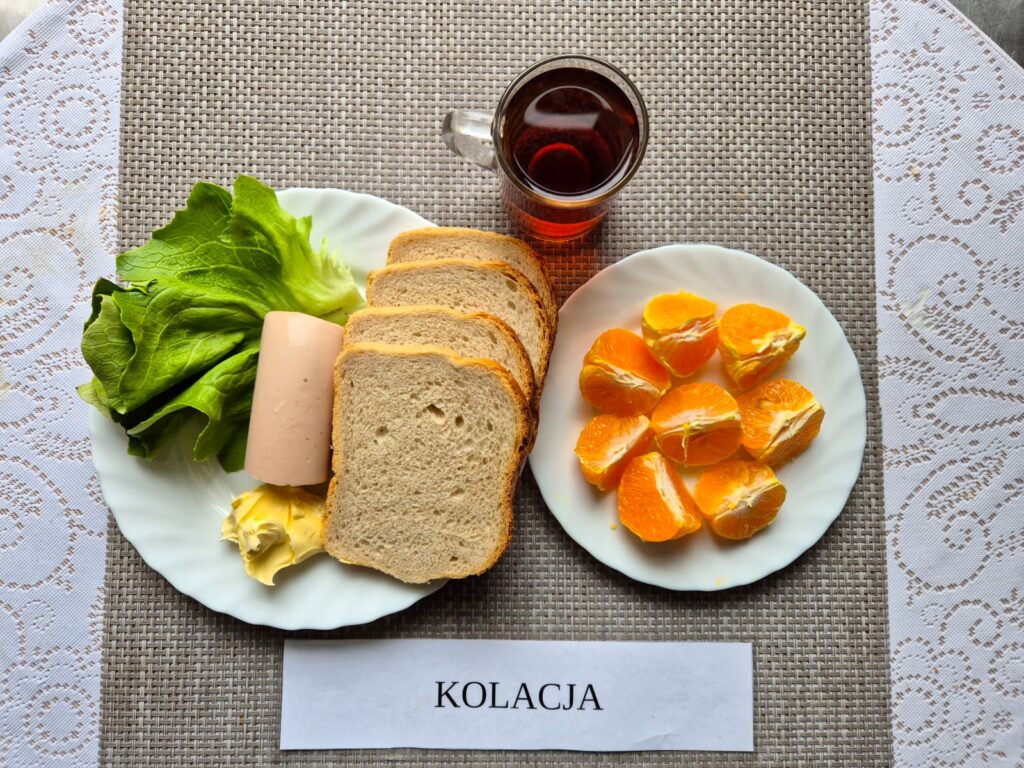 Na zdjęciu znajduję się posiłek w którego skład wchodzi Chleb razowy, Margaryna Śniadaniowa, pasta z szynki z pomidorami, Sałata masłowa, mandarynki oraz Herbata czarna