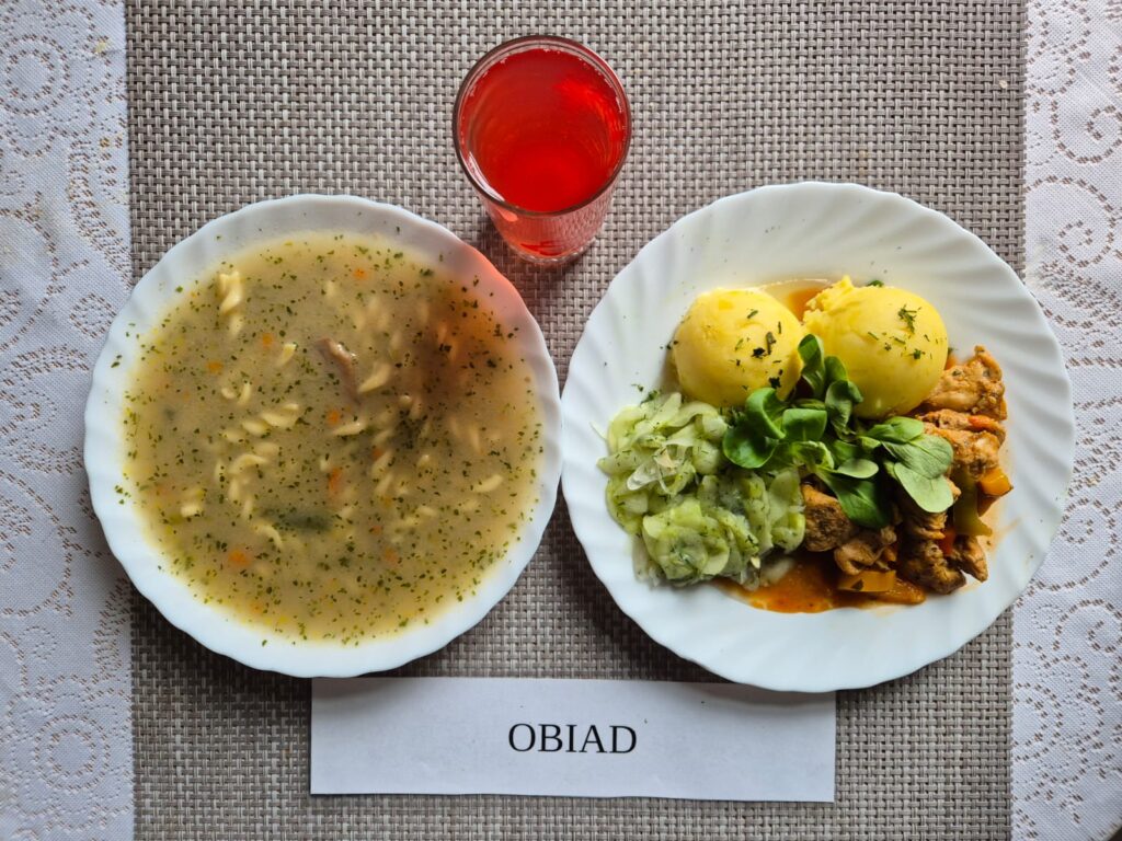 Na zdjęciu znajduję się posiłek w którego skład wchodzi Zupa pieczarkowa z makaronem, Ziemniaki gotowane, filet z indyka w sosie paprykowym, mizeria z octem oraz Kompot z jabłek