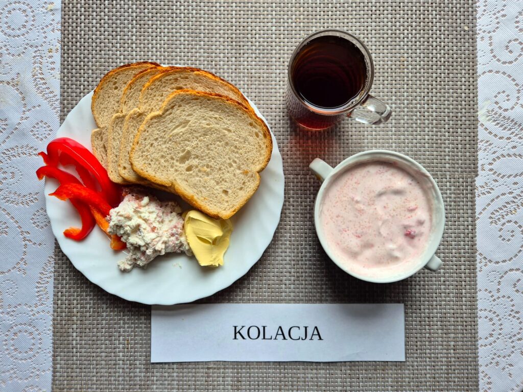 Na zdjęciu znajduję się posiłek w którego skład wchodzi Chleb pszenny, Margaryna Śniadaniowa, Twarożek mięsny, papryka czerwona, Koktajl truskawkowy oraz Herbata czarna