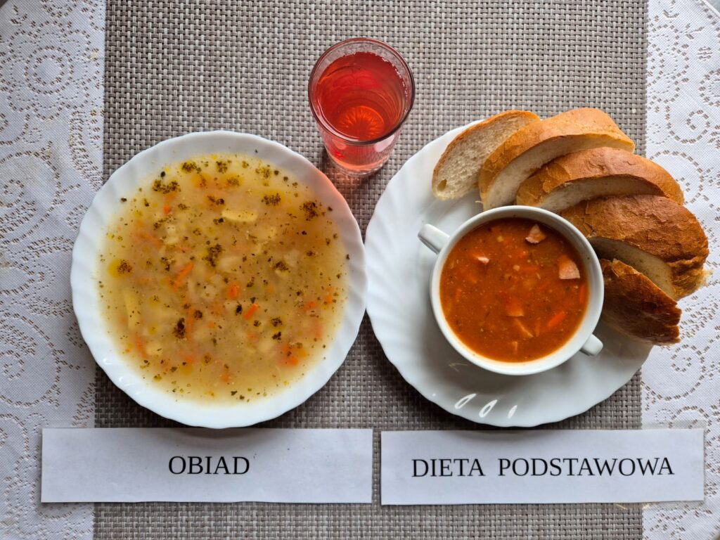 Na zdjęciu znajduję się posiłek w którego skład wchodzi Żurek z ziemniakami, Bigos, bułka pszenna oraz kompot