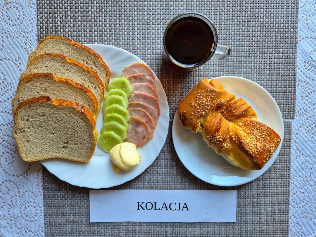 Na zdjęciu znajduję się posiłek w którego skład wchodzi Chleb pszenny, margaryna śniadaniowa, wędlina wieprzowa, pomidor oraz Herbata czarna