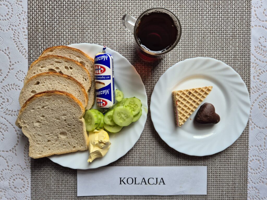 Na zdjęciu znajduję się posiłek w którego skład wchodzi Chleb pszenny, Margaryna Śniadaniowa, Ser topiony, Ogórek zielony oraz Herbata czarna