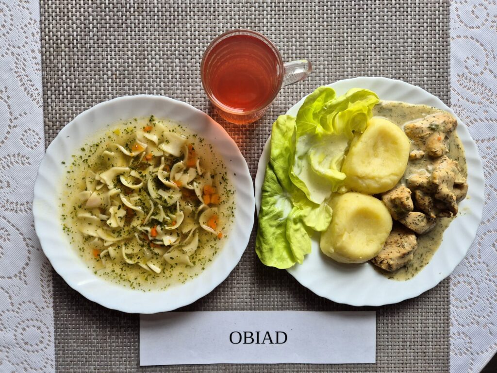 Na zdjęciu znajduję się posiłek w którego skład wchodzi Zupa jarzynowa z makaronem, Filet z kurczaka pieczony, Ziemniaki, Sałata masłowa z dodatkiem śmietany oraz Kompot z jabłek