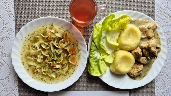 Na zdjęciu znajduję się posiłek w którego skład wchodzi Zupa jarzynowa z makaronem, Filet z kurczaka pieczony, Ziemniaki, Sałata masłowa z dodatkiem śmietany oraz Kompot z jabłek