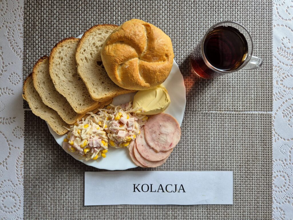 Na zdjęciu znajduję się posiłek w którego skład wchodzi Chleb pszenny, margaryna śniadaniowa, Sałata z selera z dodatkiem szynki konserwowej, kukurydzy i ananasa oraz Herbata czarna