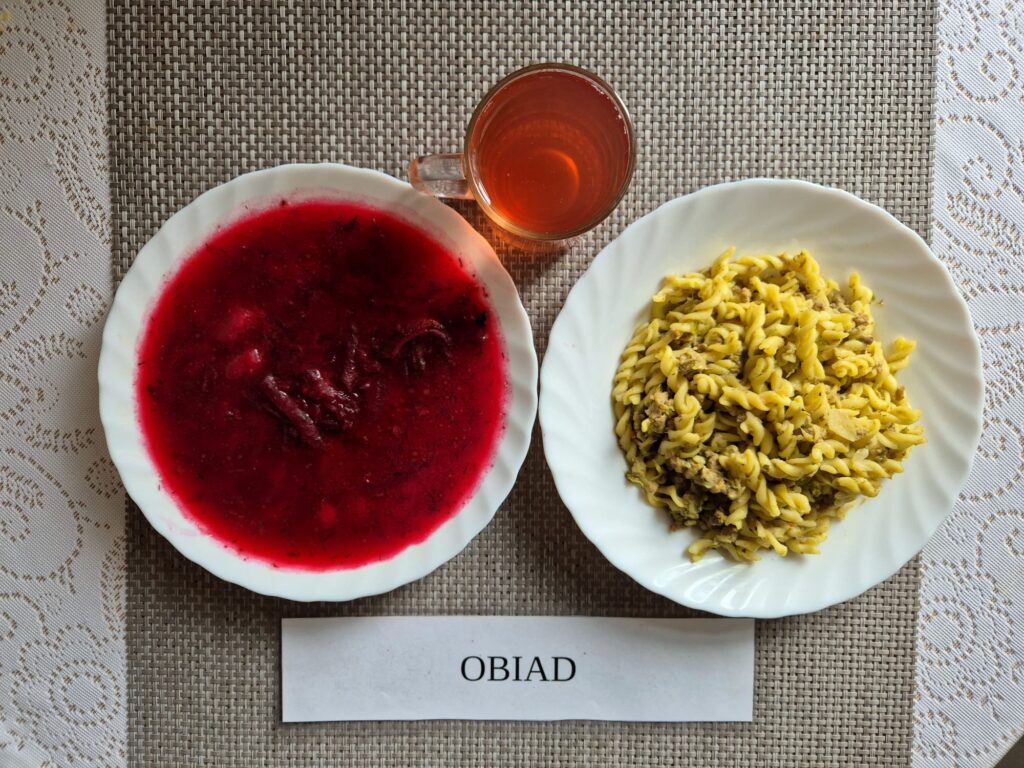 Na zdjęciu znajduję się posiłek w którego skład wchodzi Barszcz ukraiński z ziemniakami i fasolą białą, Łazanki z dodatkiem mięsa wieprzowego oraz kompot