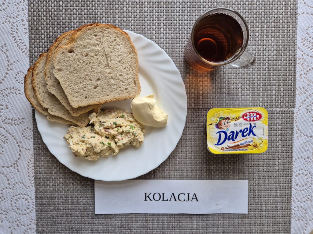 Na zdjęciu znajduję się posiłek w którego skład wchodzi Chleb pszenny, Margaryna Śniadaniowa, Jajko 2 szt z dodatkiem rzodkiewki i szczypiorku w sosie majonezowym, serek homogenizowany oraz Herbata czarna