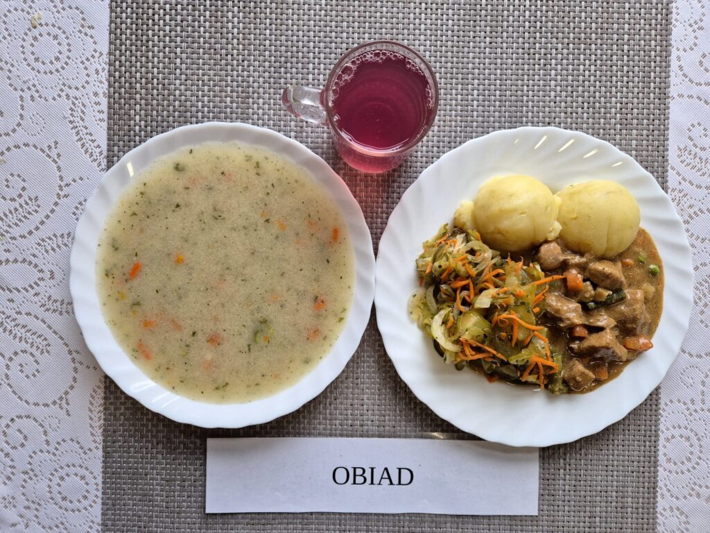 Na zdjęciu znajduję się posiłek w którego skład wchodzi Zupa grysikowa, Ziemniaki, Gulasz wieprzowy, surówka z ogórka kiszonego i marchewki oraz Kompot z jabłek
