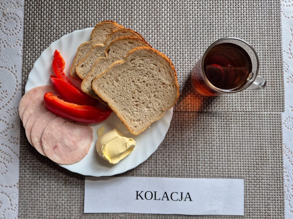 Na zdjęciu znajduję się posiłek w którego skład wchodzi Chleb pszenny, Margaryna Śniadaniowa, Kiełbasa krakowska wieprzowa, Herbata czarna