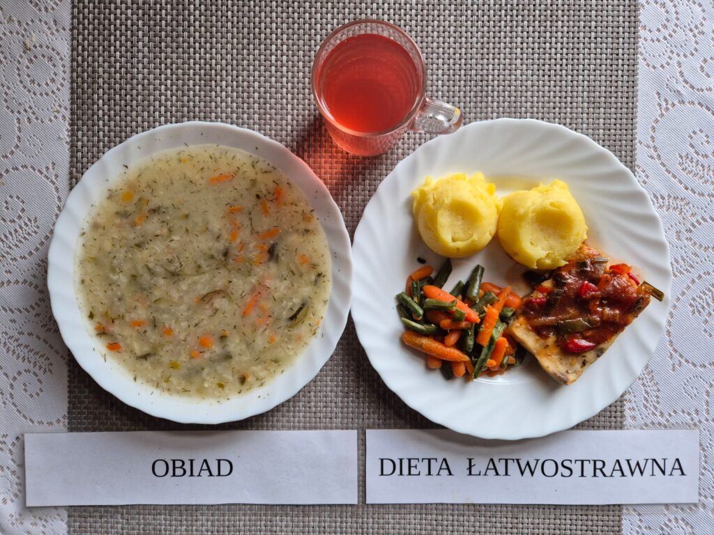 Na zdjęciu znajduję się posiłek w którego skład wchodzi Zupa ogórkowa z ryżem, Ryba pieczona w warzywach, ziemniaki, Marchewka mini oraz kompot