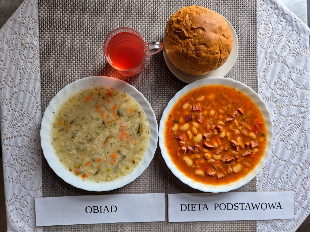 Na zdjęciu znajduję się posiłek w którego skład wchodzi Zupa ogórkowa z ryżem, fasolka po bretońsku, Bułka pszenna, kompot