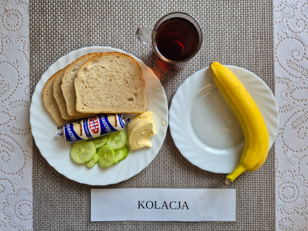 Na zdjęciu znajduję się posiłek w którego skład wchodzi Chleb pszenny, Margaryna Śniadaniowa, Ser topiony, ogórek zielony oraz Herbata czarna