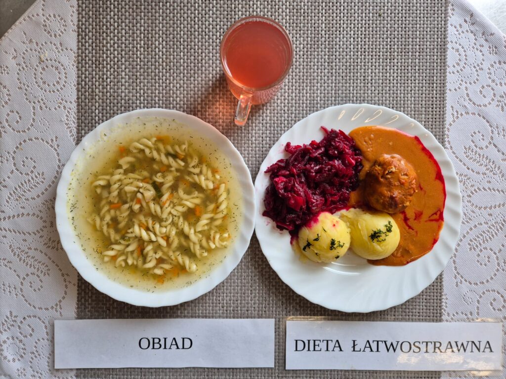 Na zdjęciu znajduję się posiłek w którego skład wchodzi Zupa jarzynowa z makaronem, Pulpet drobiowy w sosie pomidorowym, Ziemniaki, Surówka z buraka, Kompot z jabłek