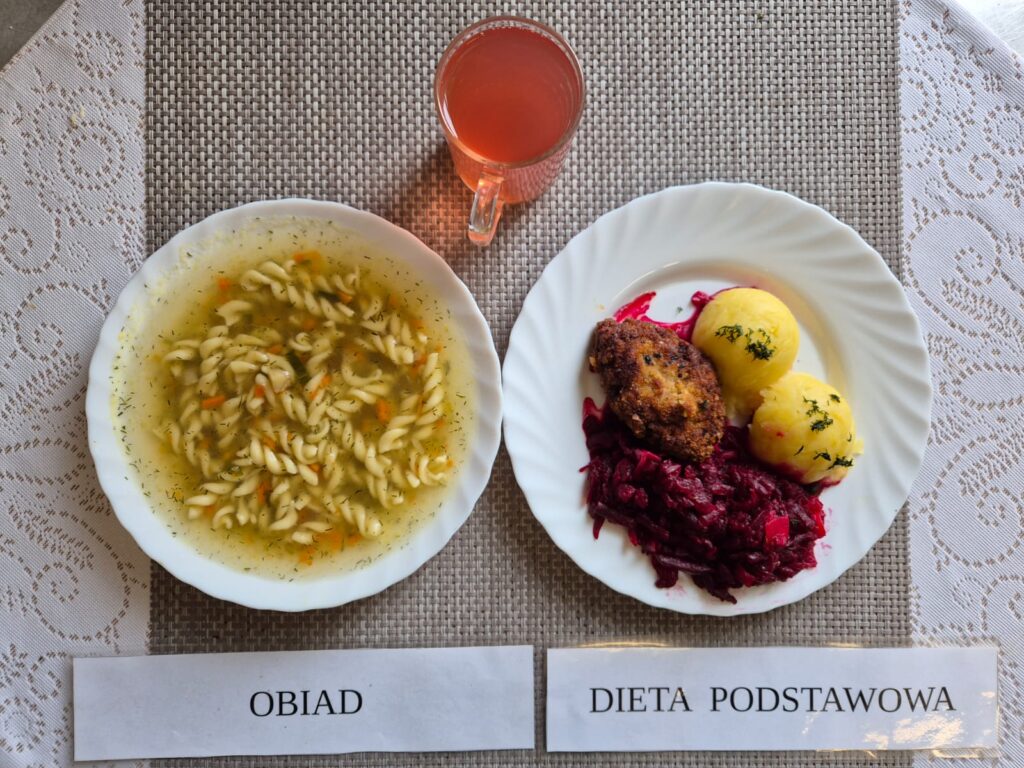 Na zdjęciu znajduję się posiłek w którego skład wchodzi Zupa jarzynowa z makaronem, Sznycel, Ziemniaki, Surówka z buraka oraz Kompot z jabłek