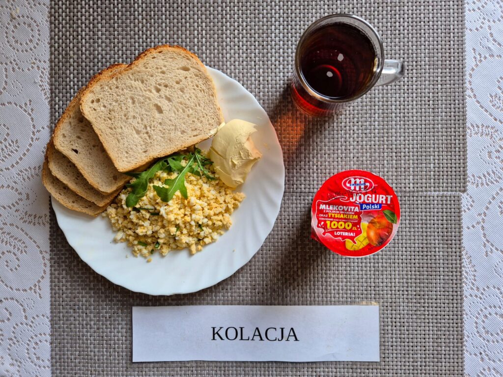 Na zdjęciu znajduję się posiłek w którego skład wchodzi Chleb pszenny, margaryna śniadaniowa, Pasta jajeczna ze szczypiorkiem oraz Herbata czarna