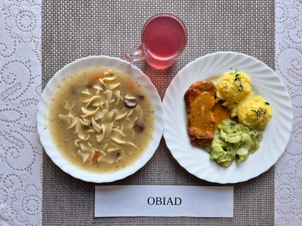 Na zdjęciu znajduję się posiłek w którego skład wchodzi Zupa pieczarkowa z makaronem, Ziemniaki, Bitka wieprzowa w sosie własnym, mizeria z octem oraz Kompot z jabłek