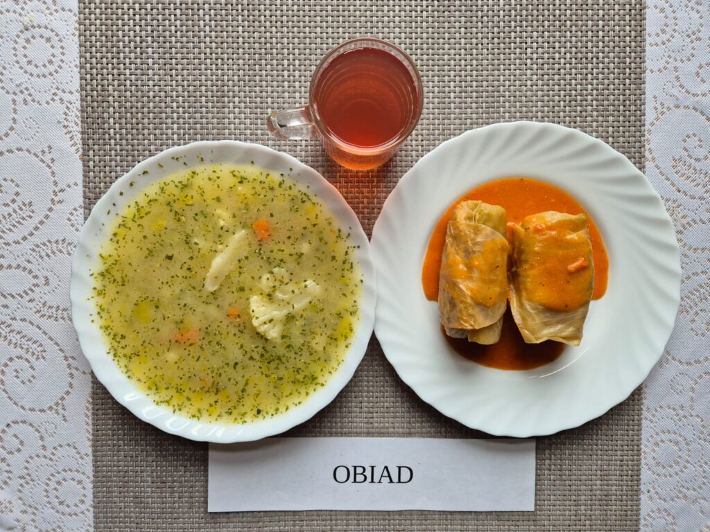 Na zdjęciu znajduję się posiłek w którego skład wchodzi Zupa kalafiorowa z ziemniakami, Gołąbki w sosie pomidorowym oraz kompot z jabłek
