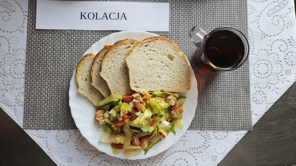 Na zdjęciu znajduję się posiłek w którego skład wchodzi Chleb pszenny, margaryna śniadaniowa, Sałata gyros, Herbata czarna