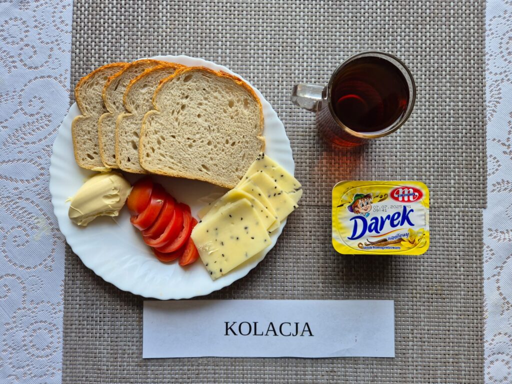 Na zdjęciu znajduję się posiłek w którego skład wchodzi Chleb pszennym Margaryna Śniadaniowa, Ser twardy, pomidor, serek homogenizowany oraz Herbata czarna