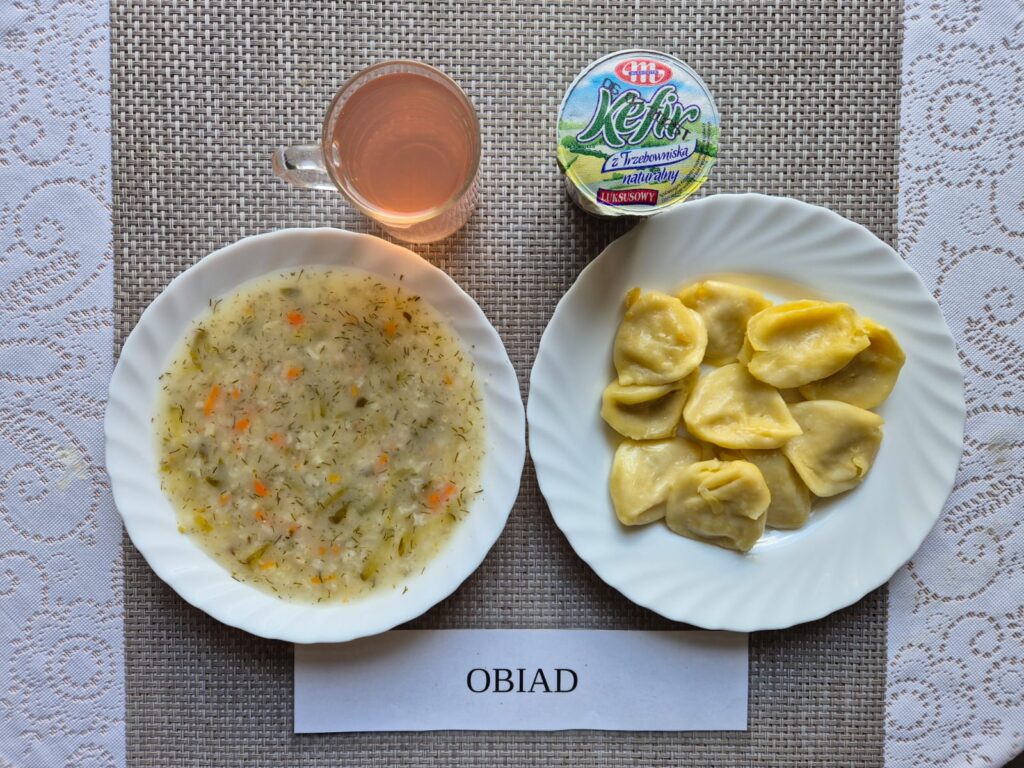 Na zdjęciu znajduję się posiłek w którego skład wchodzi Zupa ogórkowa z ryżem, Pierogi 10 szt., kefir oraz kompot z jabłek